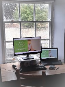 Photo of a desk in front of a window with a laptop and monitor