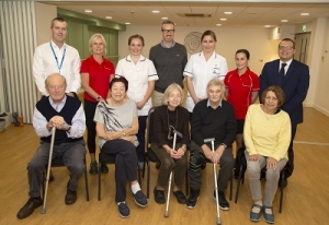 Group of people - older people with walking sticks sat down in front of a group of workers