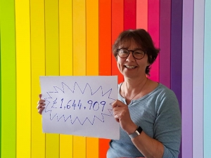 Emma Lower of Lendology CIC in front on a colourful background holding a sign saying £1,644,909