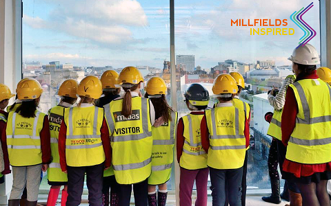 Photo of schoolchildren wearing hard hats and high vis jackets looking out of a window across a cityscape