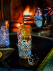 Gin being poured into a highball glass with a fire in the background
