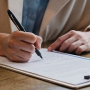 A person holding a pen over paper on a clipboard
