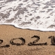 Image of 2021 written in sand with the tide coming in over the sand
